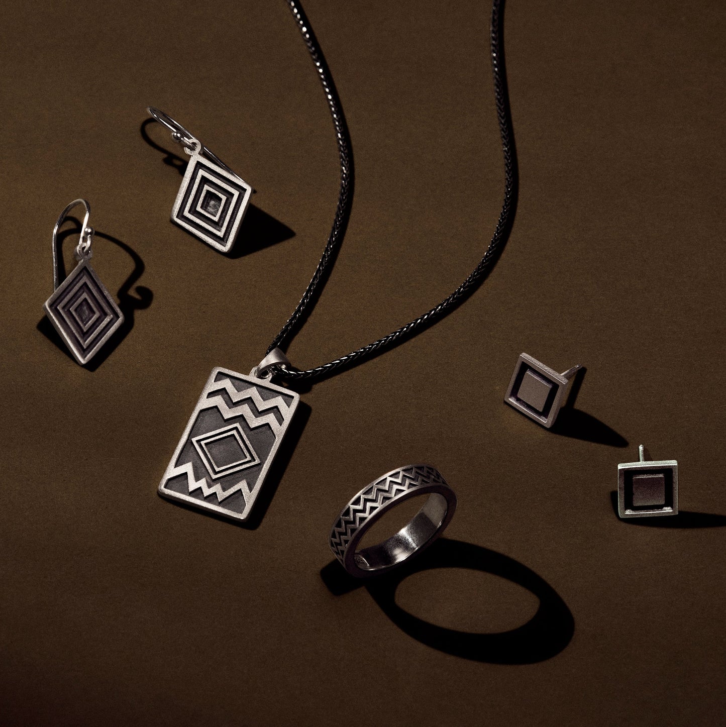 Silver ring jewelry collection with the ring, pendant, earrings inspired by Maya Hieroglyphs with satin oxidized finish on an earthy green background