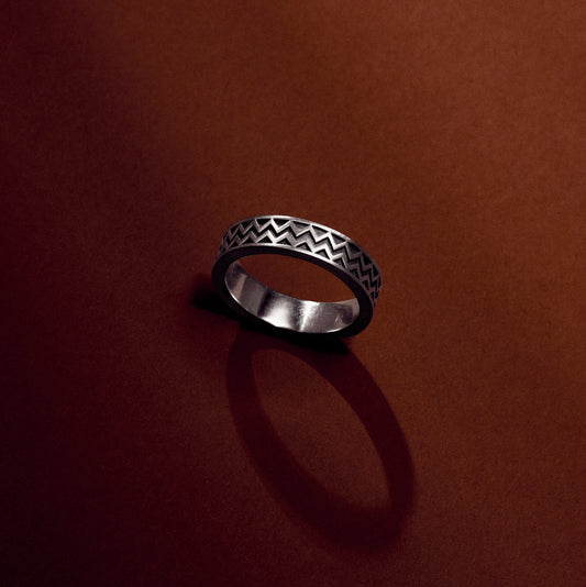 Silver ring with a chevron pattern referencing Maya Hieroglyphs with satin oxidized finish on an earthy terracotta  background